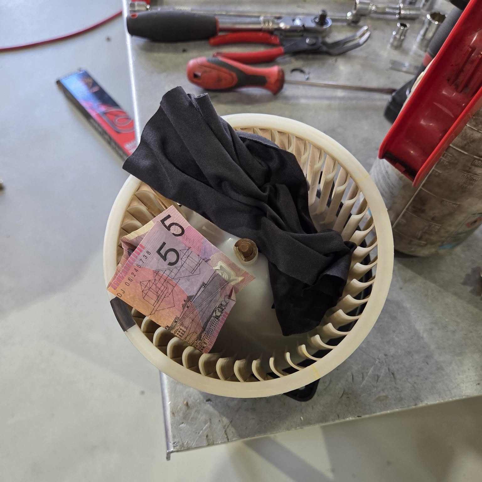 An Australian five dollar note and a black rag pulled out of a heater blower fan on the workbench